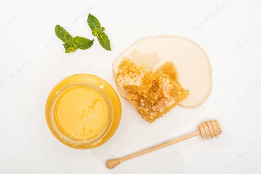 top view of jar with honey, mint, honeycomb and wooden dipper on white background