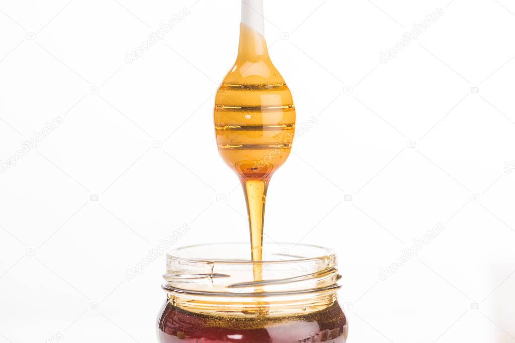 jar with dripping honey and wooden honey dipper isolated on white 