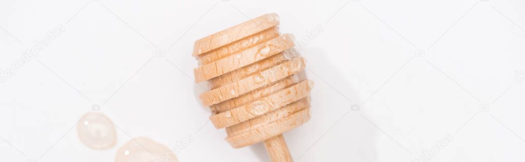 panoramic shot of honey drops and wooden honey dipper on white background