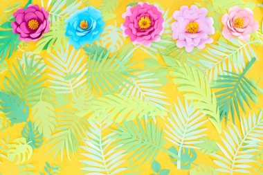 flat lay with paper cut multicolored flowers on tropical leaves on yellow bright background with copy space clipart
