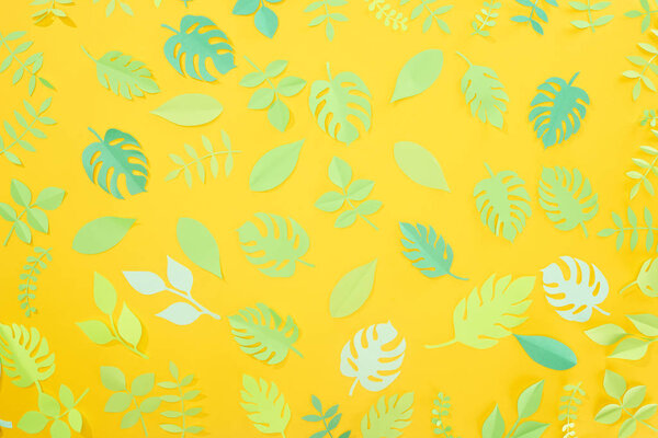 top view of paper cut green tropical leaves on yellow bright background