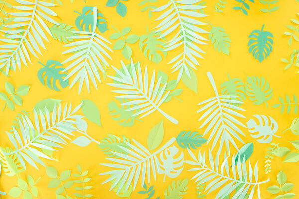 top view of paper cut green tropical leaves on yellow bright background with copy space