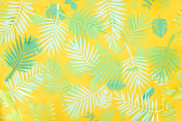 top view of paper cut green tropical leaves on yellow bright background with copy space