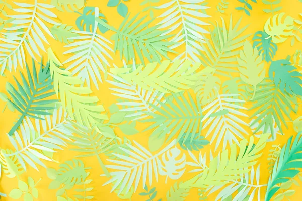 top view of paper cut green tropical leaves on yellow bright background with copy space