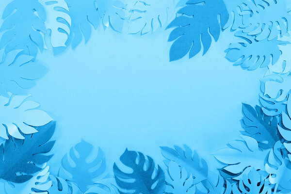 frame of paper cut exotic leaves on blue minimalistic background with copy space