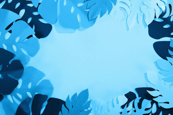 top view of paper cut tropical leaves on blue minimalistic background with copy space