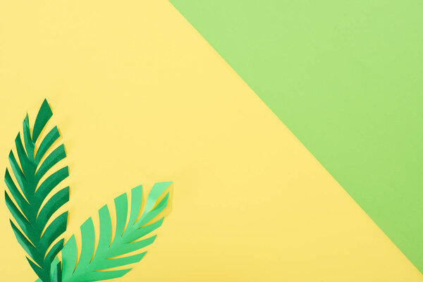 top view of paper cut palm leaves on yellow and green bright background with copy space