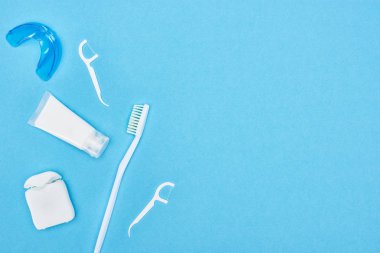 top view of toothbrush, toothpaste and teeth floss near retainer isolated on blue  clipart