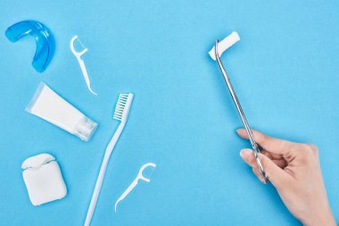 cropped view of woman holding tweezers with cotton pad near toothpaste and toothbrush on blue  clipart