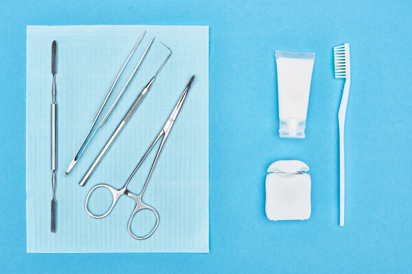 top view of set with dental tools near toothpaste and toothbrush isolated on blue 