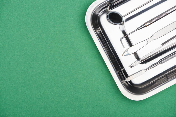 top view of set with dental instruments in metallic plate isolated on green 