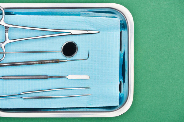 top view of set with dental tools in metallic plate isolated on green 
