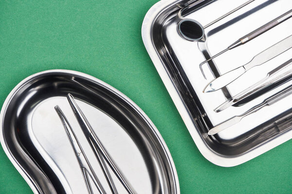 top view of set with dental tools in metallic plates isolated on green 