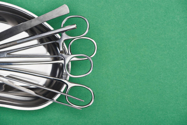 top view of scissors and dental tools in metallic plate isolated on green 