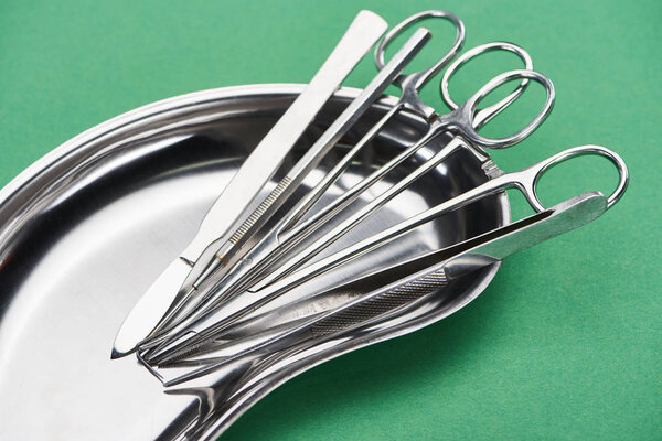 scissors and dental instruments in metallic plate isolated on green 