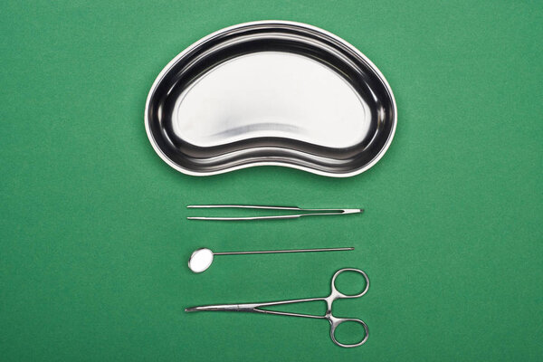 top view of scissors and dental instruments near metallic plate isolated on green 
