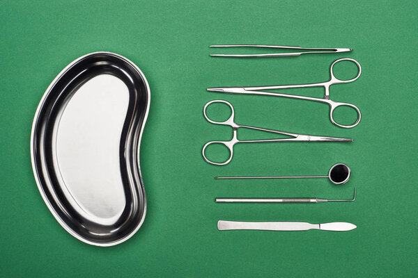 top view of metallic plate near set with dental tools and scissors isolated on green 