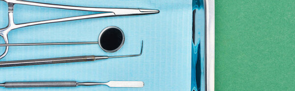 panoramic shot of set with dental tools in metallic plate isolated on green 