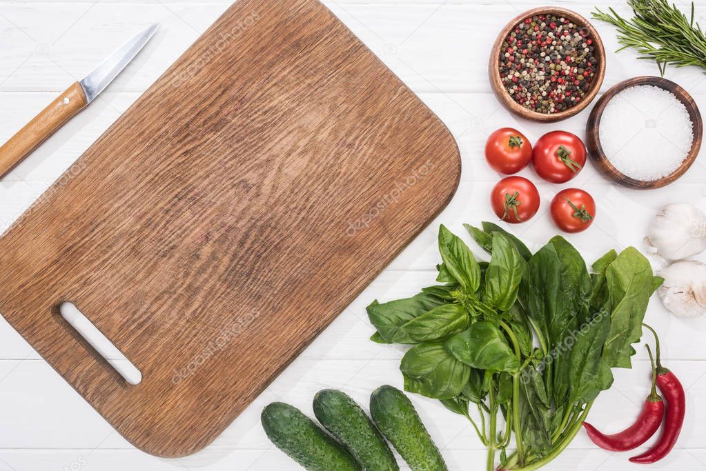 top view of cutting board, cherry tomatoes, greenery, chili peppers, salt, cucumbers, knife, garlics and spices 