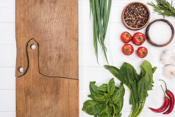 top view of cutting boards, cherry tomatoes, greenery, chili peppers, salt, garlics and spices 