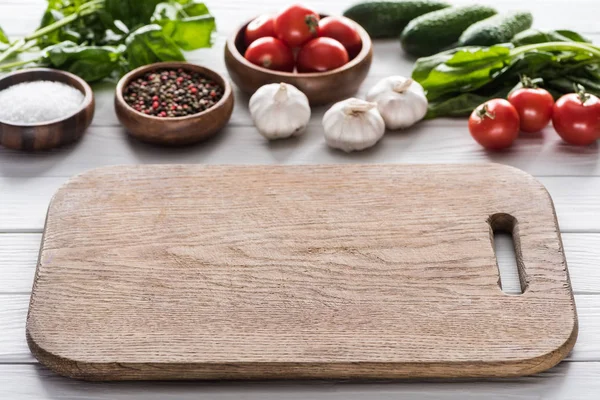 selective focus of cutting board, cherry tomatoes, greenery, garlics, cucumbers, salt and spices 