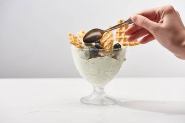 gri üzerinde izole waffle ve yaban mersini ile fıstıklı dondurma ile kase yakın kadın tutan kaşık kırpılmış görünümü