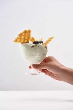 cropped view of woman holding delicious pistachio ice cream with waffles and blueberries isolated on grey clipart