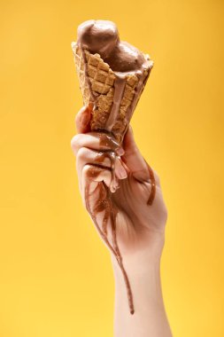 sarı üzerinde izole çıtır waffle koni lezzetli erimiş çikolata dondurma tutan kadının kısmi görünümü