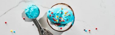 Hindistan cevizi yarısında Sprinkles ile lezzetli mavi dondurma üst görünümü ve mermer gri arka plan üzerinde dondurma kaşığı, panoramik çekim