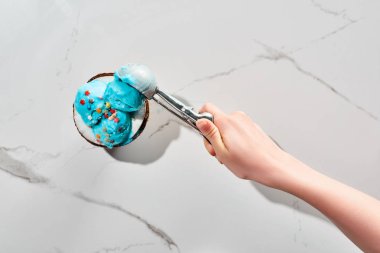 mermer gri arka plan üzerinde kaşık ile Hindistan cevizi yarısında Sprinkles ile lezzetli mavi dondurma alarak kadının kırpılmış görünümü