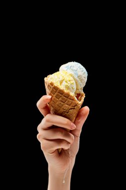 cropped view of woman holding delicious vanilla ice cream with sprinkles in crispy waffle cone isolated on black  clipart