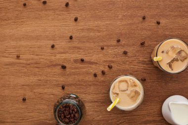 top view of ice coffee in glasses with straw, milk and coffee grains on wooden table clipart