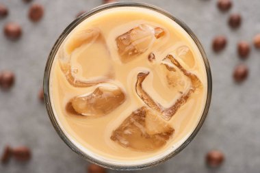close up view of ice coffee in glass with straw and coffee grains on grey background clipart