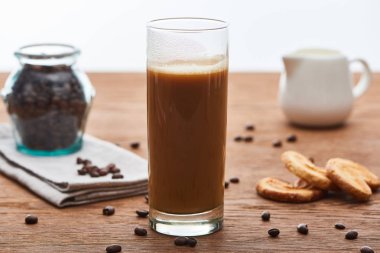 beyaz üzerinde izole ahşap masa üzerinde süt sürahi, kurabiye ve kahve taneleri yakın cam süt ile buz kahve seçici odak