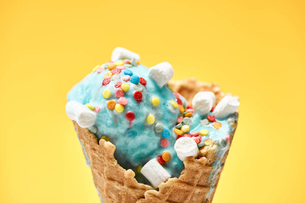 close up view of delicious sweet blue ice cream with marshmallows and sprinkles in crispy waffle cone isolated on yellow