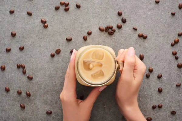 灰色の背景にアイスコーヒーとコーヒーの穀物とガラス瓶を保持している女性のトリミングビュー — ストック写真