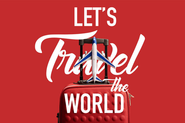 red colorful textured travel bag with plane model isolated on red with lets travel the world illustration