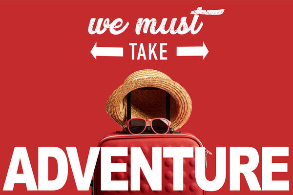 red colorful travel bag with straw hat and sunglasses isolated on red with we must take adventure illustration