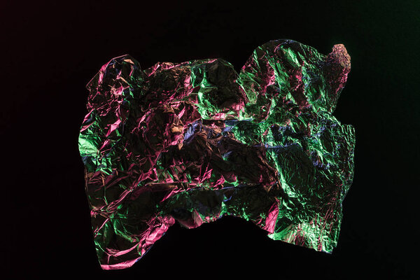 top view of crumpled foil with colorful lighting reflection in darkness isolated on black