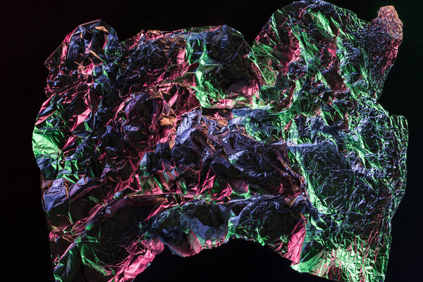 top view of crumpled foil with colorful reflection in darkness isolated on black