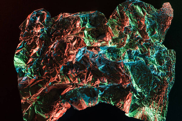 top view of shiny crumpled foil with colorful lighting reflection in darkness isolated on black