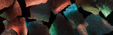 panoramic shot of abstract background of ragged foil with colorful illumination isolated on black clipart
