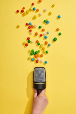 cropped view of woman holding microphone with colorful candies on yellow background  clipart