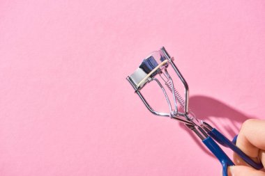pembe arka plan üzerinde kirpik curler tutan kadın kırpılmış görünümü