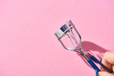 cropped view of woman holding eyelash curler on pink background