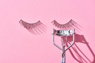 top view of false eyelashes and eyelash curler on pink background  clipart