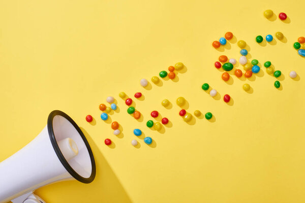 top view of loudspeaker with colorful candies on yellow background 