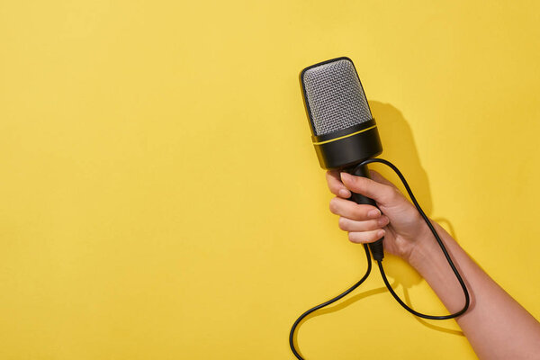 cropped view of woman holding microphone on yellow background 