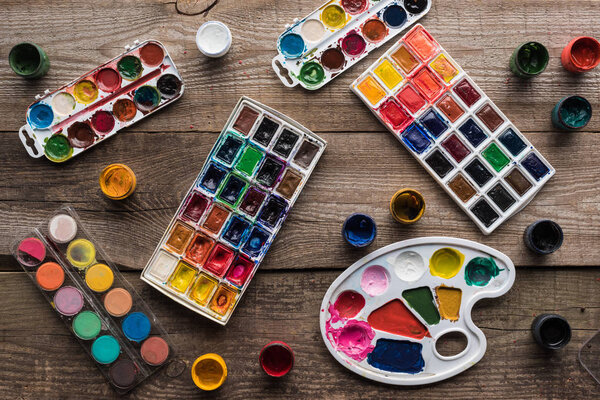 top view of colorful paint palettes and gouache on wooden brown surface