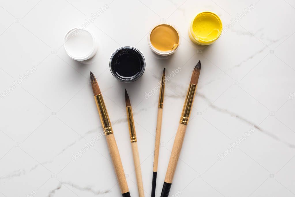 top view of gouache paints and paintbrushes on marble white surface